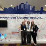 Zoe (left, Dominic (middle), and Hannah (right) posing for a picture at the ACS Proud to be a Chemist writing wall at the conference